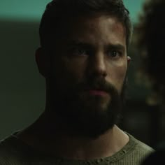 a man with a beard stares into the distance while standing in front of another man