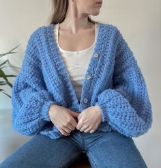 a woman sitting on top of a wooden chair wearing a blue cardigan sweater and jeans