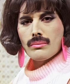 a close up of a person wearing pink earrings and a moustache on their face