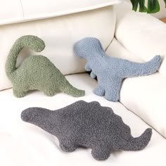 three stuffed dinosaurs sitting on a white couch