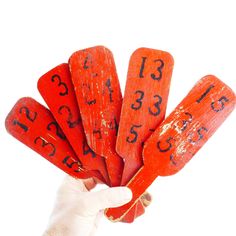 a hand is holding five red wooden numbers on sticks with numbers painted on them,