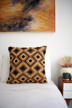 a bed with white sheets and a painting on the wall above it that has an abstract design