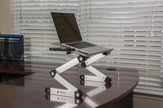 a laptop computer sitting on top of a wooden table next to a window with blinds