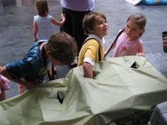 several children standing around looking at something in a bag on the ground with adults nearby