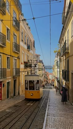 a yellow trolley car traveling down a street next to tall buildings with balconies