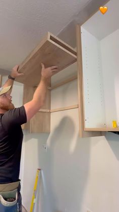 a man is working on the cabinets in his kitchen, with one hand reaching for the shelf