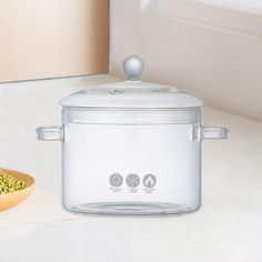 a glass crock pot sitting on top of a counter next to a wooden spoon