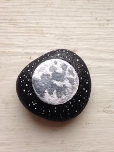 a rock with a white and black moon painted on it sitting on top of a wooden table