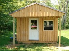 a small wooden shed with a white door and window in the grass next to trees