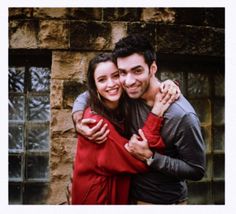 a man and woman hugging each other in front of a brick wall