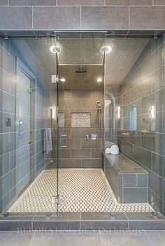 a walk in shower sitting next to a tiled wall and floor covered in gray tiles