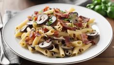 a white plate topped with pasta covered in bacon, mushrooms and green peppers next to a fork