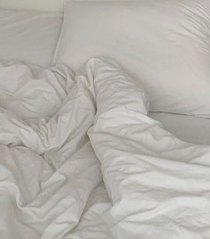 an unmade bed with white sheets and pillows