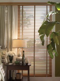 a bed room with a neatly made bed next to a window covered in blinds and pillows