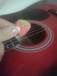 someone is playing an acoustic guitar with a strawberry sticker on their fingernails