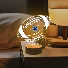 a lamp that has a football on it next to a night stand with a bed in the background