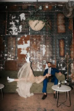 a man and woman sitting on a couch in front of a wall with peeling paint