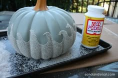 a white pumpkin sitting on top of a tray next to a bottle of glue and some snow