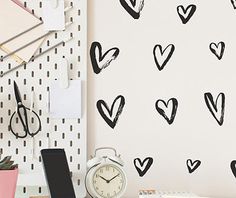 a desk with a clock, phone and other office supplies on it in front of a wall with hearts drawn on it