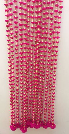 pink and gold beaded wall hanging with pom poms on the bottom half