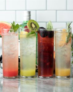 four different types of drinks are lined up on the counter with limes, watermelon and kiwi