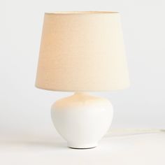 a white table lamp with a beige shade on the base and a cord attached to it