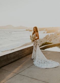 a woman in a wedding dress standing on the edge of a cliff by the ocean