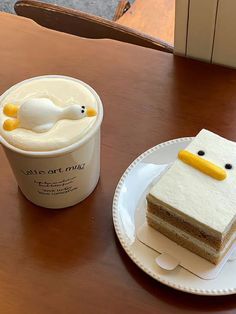 a piece of cake on a plate next to a cup of coffee with a ducky face