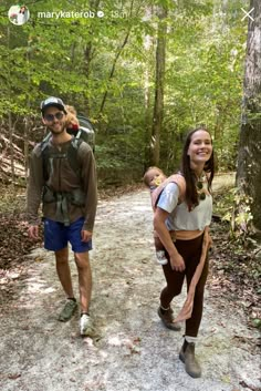 a man and woman walking down a dirt road in the woods with backpacks on