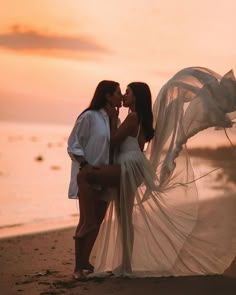 two beautiful women standing next to each other on a beach at sunset with veil blowing in the wind