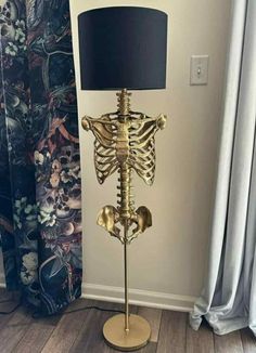 a gold skeleton lamp with a black shade on the floor in front of a window