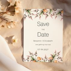 a wedding save the date card with flowers on it next to a bouquet of white flowers