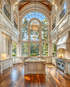 a large kitchen with wooden floors and an arched window above the island is surrounded by white cabinetry