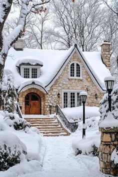 a stone house covered in snow next to trees and steps leading up to the front door