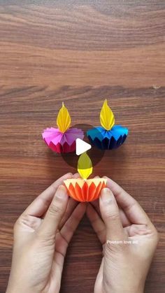 someone is holding up some paper flowers on a wooden surface with their hands and fingers