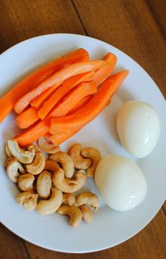 carrots, cashews and an egg on a white plate with wood table