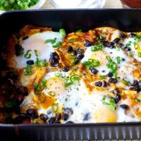 an enchilada dish with black beans, cheese and green onions in a casserole dish