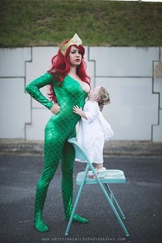 a woman in a green mermaid costume is holding a child on a blue lawn chair