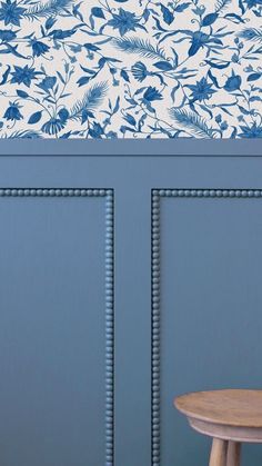 a wooden stool sitting in front of a blue wall with floral designs on the walls