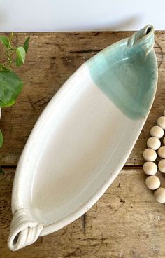 a white and blue ceramic platter next to some green leaves on a wooden table