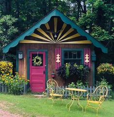 two yellow chairs and a table in front of a small shed with flowers on it