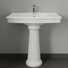 a white pedestal sink sitting on top of a tiled floor next to a gray wall