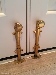 two golden door handles are standing next to each other on the floor near a white door