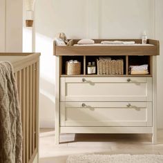 a baby's crib in a room with white walls and wooden furniture, including a changing table