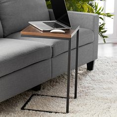 a laptop computer sitting on top of a wooden table next to a gray couch in a living room