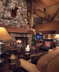 a living room filled with furniture and a fire place next to a stone wall covered in deer heads