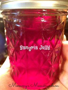 a hand holding a pink glass jar with the name sangria jelly written on it