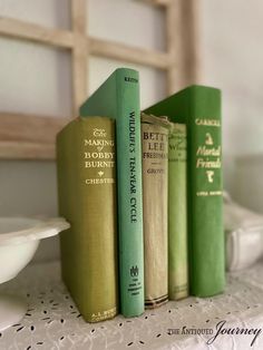 three books sitting on top of a table next to a white bowl and wooden framed window