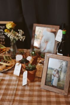 a table topped with pictures and potted plants next to a bottle of wine on top of a checkered table cloth