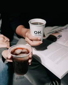 a person holding a drink in their hand and an open book on the table behind them